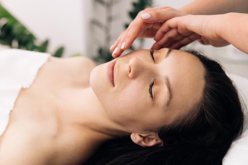 En ung kvinna ligger avslappnat på en massagebänk i en skönhetssalong och mottar en professionell ansiktsmassage