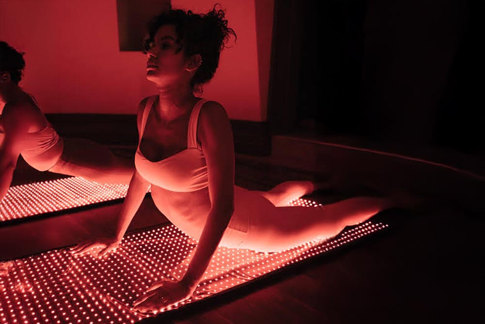 En kvinna sitter på en IR madrass som lyser i intensivt rött ljus med ett mönster av vita prickar